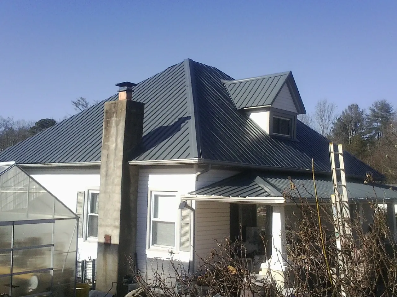 Dark blue standing seam metal roof on a white farmhouse with dormer — Slate & Tile Roof Repair by Roofing Brothers in Bellvue