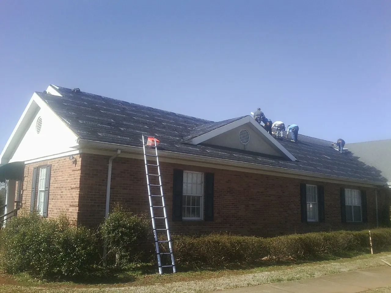 Crew tearing shingles off a brick ranch roof with a ladder set — Emergency Roof Repair work by our crew in Bellvue