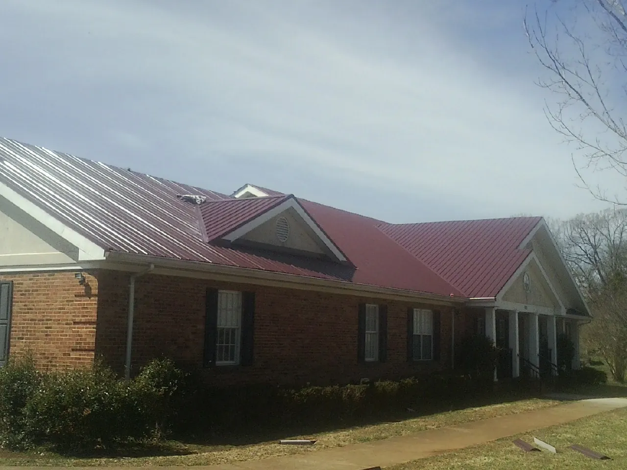 Red metal roof with gabled entries on a long brick building, from a Hail Damage Roof Repair job in Bellvue