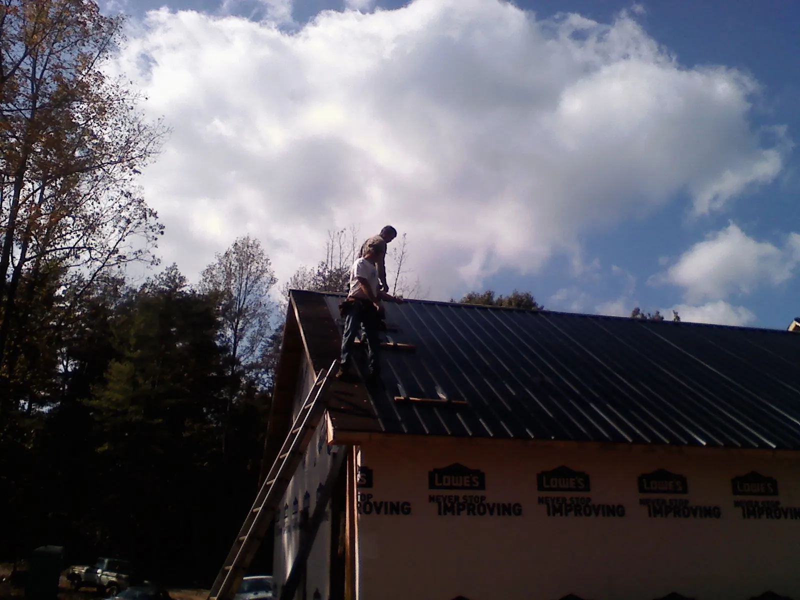 Roofer fastening dark metal panels high against a cloudy sky, from a Roof Inspection job in Bellvue