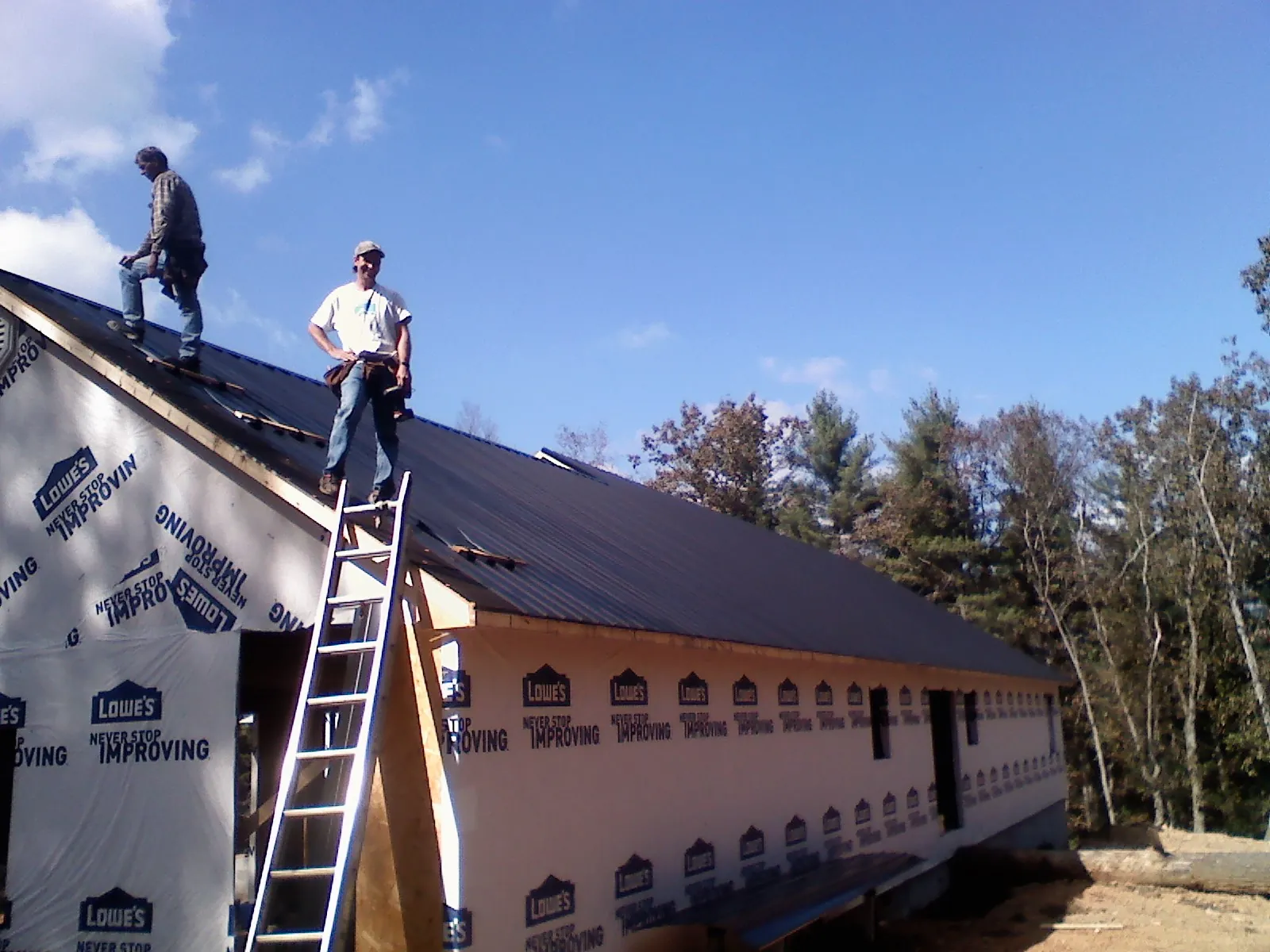 Two roofers standing on a long dark metal roof over a wrapped building in Bellvue
