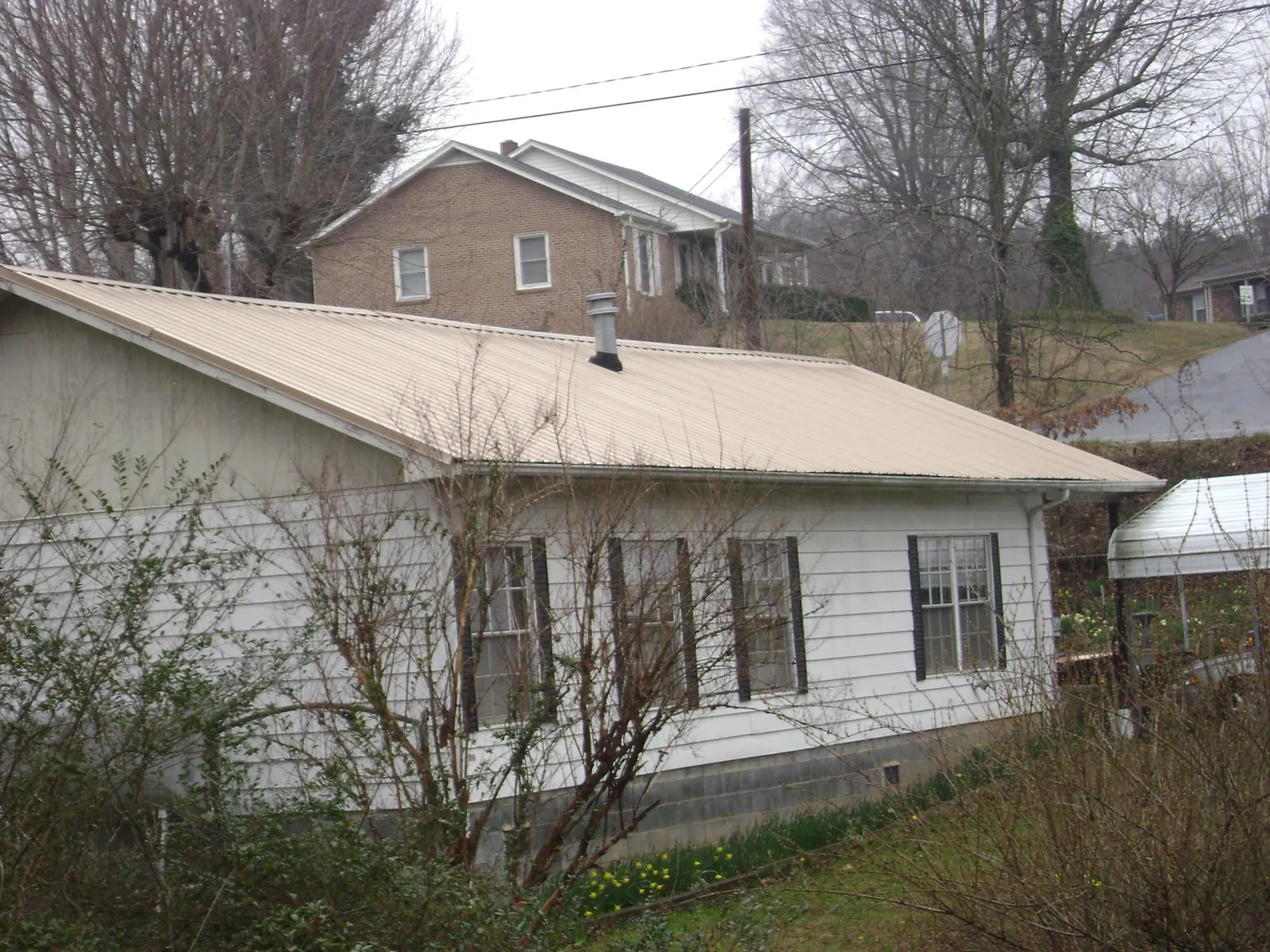Tan metal roof on a white sided house set into a hillside — Commercial Roofing by Roofing Brothers in Bellvue